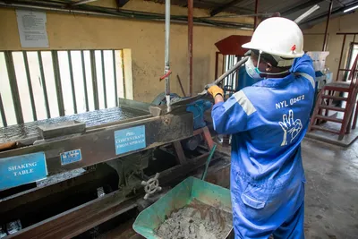 A factory worker in blue overalls operates a shaking table for ore processing.