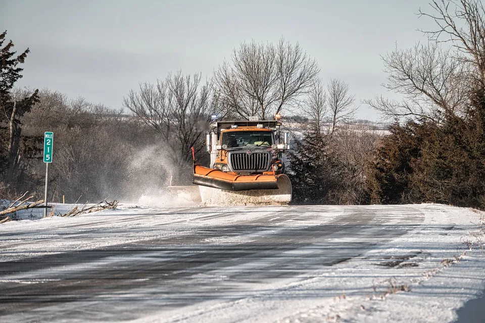 A snowplow clears a rural road in winter, showcasing winter maintenance.
