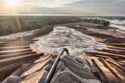 Drone shot of sand processing with flowing water and forest backdrop in Reads Landing, MN, at sunset.